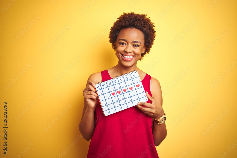 Young african american woman holding menstruation calendar over isolated yellow background with a happy face standing and smiling with a confident smile showing teeth - obrazy, fototapety, plakaty 