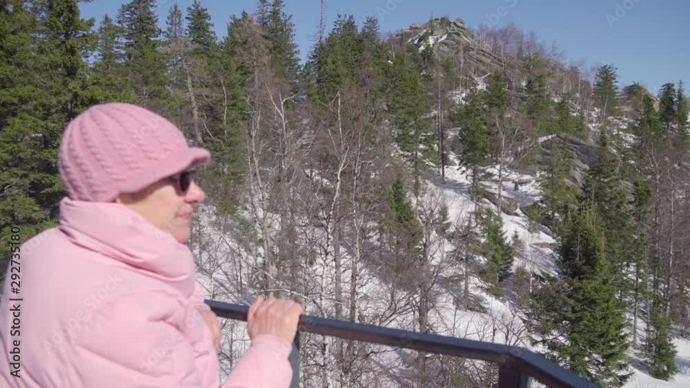 An aged woman looks at the unprecedented beauty of winter. Grandmother breathes fresh air in nature.
