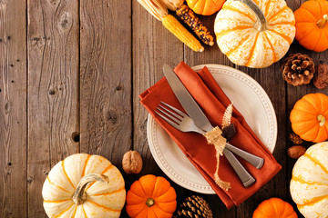 Autumn harvest or thanksgiving table setting with silverware, orange napkin, pumpkins and decor. Top view, corner border against a rustic wood background.