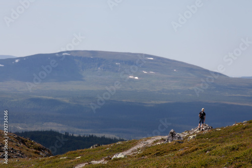Young boy looks out over the mountain valley. Shallow depth of field. Blurred mountainside in the distance. Blue sky on a nice summer day.