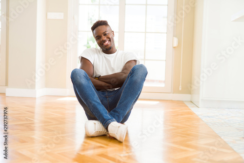 Handsome african american man sitting on the floor at home happy face smiling with crossed arms looking at the camera. Positive person. © Krakenimages.com