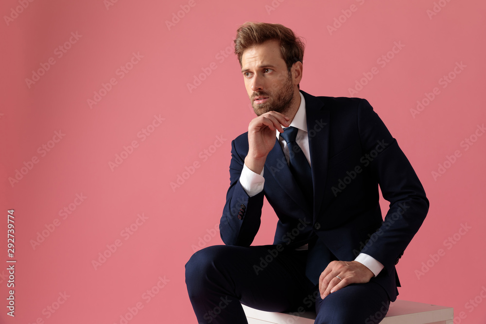 businessman sitting and touching his chin while looking away pensive businessman sitting and touching his chin while looking away pensive
