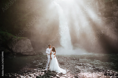 Young couple in love bride and groom, wedding day near a mountain waterfall. Enjoy a moment of happiness and love. Bride in a luxurious wedding dress