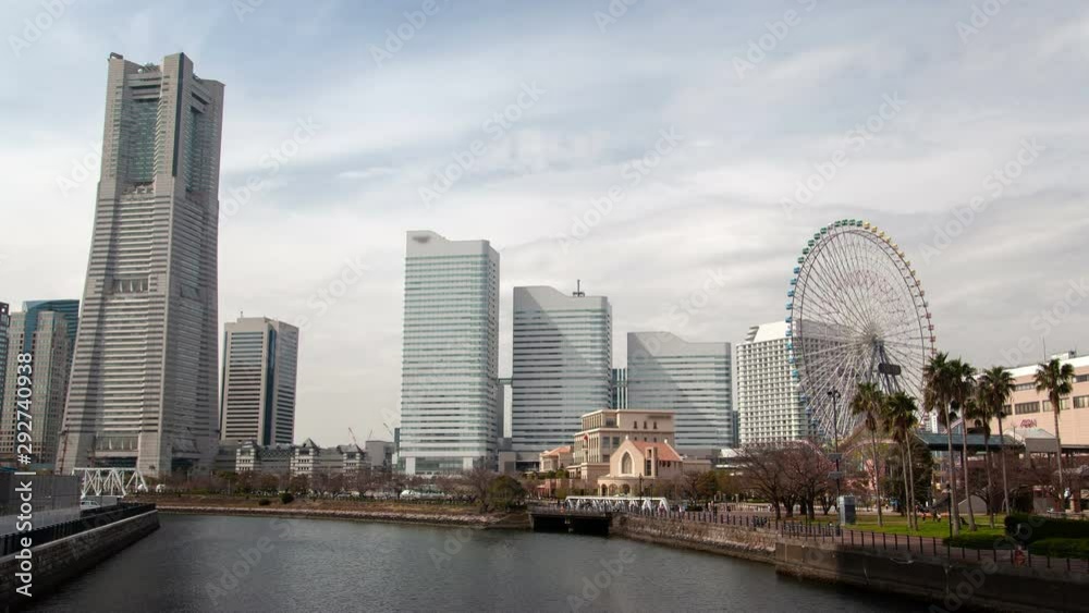 Timelapse zoom out Yokohama sea waterfront with park entertainment attraction Ferris wheel and people flow against metropolis downtown skyscrapers of contemporary architecture under floating clouds Timelapse zoom out Yokohama sea waterfront with park entertainment attraction Ferris wheel and people flow against metropolis downtown skyscrapers of contemporary architecture under floating clouds