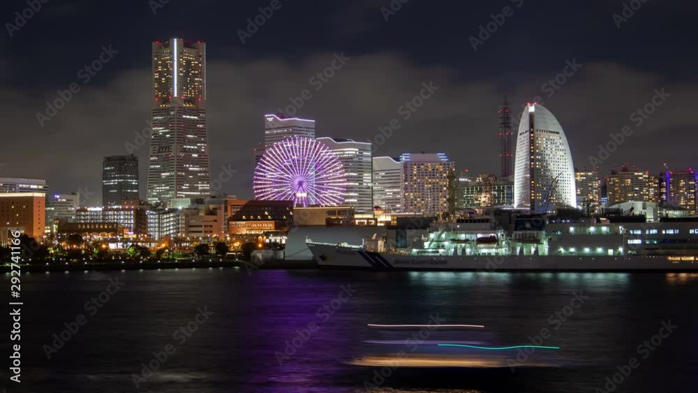 Timelapse zoom out Yokohama seafront at night illumination with Japanese popular entertainment Ferris wheel changing colors by highrise white tower against downtown skyscrapers reflected on bay water Timelapse zoom out Yokohama seafront at night illumination with Japanese popular entertainment Ferris wheel changing colors by highrise white tower against downtown skyscrapers reflected on bay water