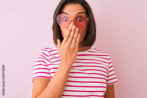 Young beautiful woman wearing fashion sunglasses with hearts over isolated pink background cover mouth with hand shocked with shame for mistake, expression of fear, scared in silence, secret concept