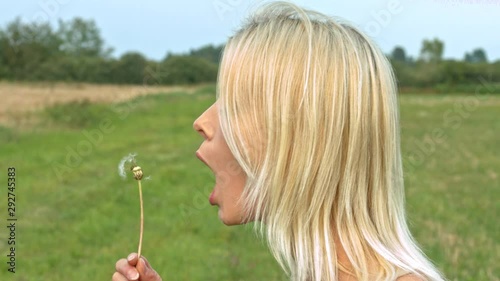 Profile side view of young woman blowing dandelion seeds in a field meadow