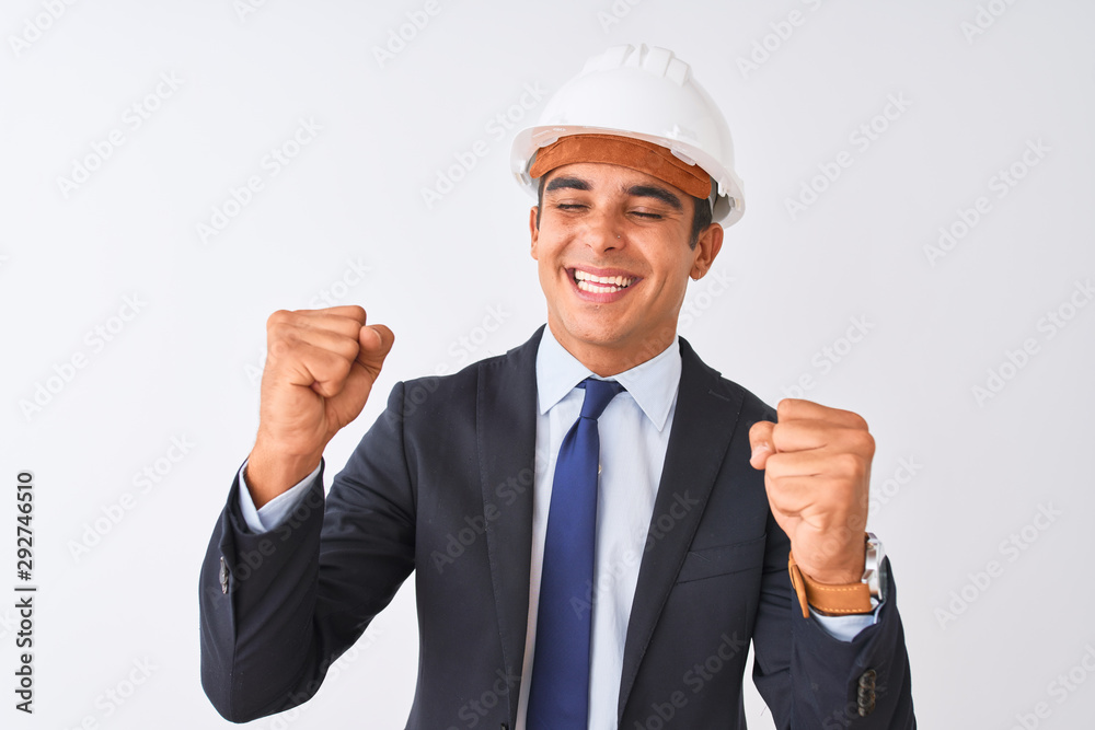 Young handsome architect man wearing suit and helmet over isolated white background very happy and excited doing winner gesture with arms raised, smiling and screaming for success Young handsome architect man wearing suit and helmet over isolated white background very happy and excited doing winner gesture with arms raised, smiling and screaming for success