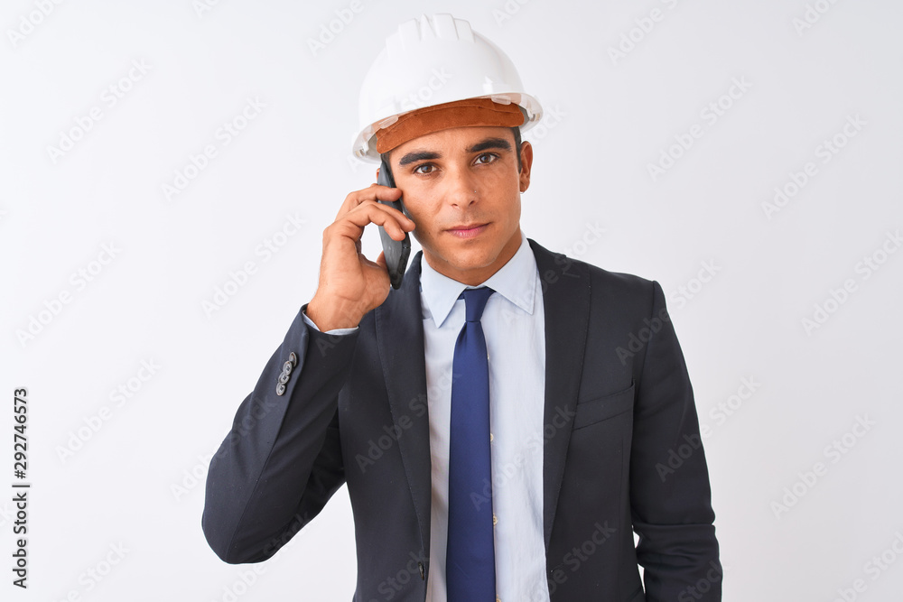 Young architect man wearing helmet talking on smartphone over isolated white background with a confident expression on smart face thinking serious Young architect man wearing helmet talking on smartphone over isolated white background with a confident expression on smart face thinking serious