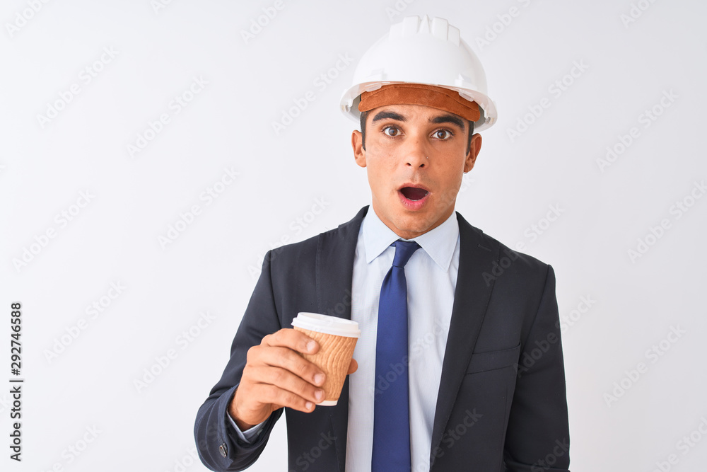 Young handsome architect man wearing helmet drinking coffee over isolated white background scared in shock with a surprise face, afraid and excited with fear expression Young handsome architect man wearing helmet drinking coffee over isolated white background scared in shock with a surprise face, afraid and excited with fear expression