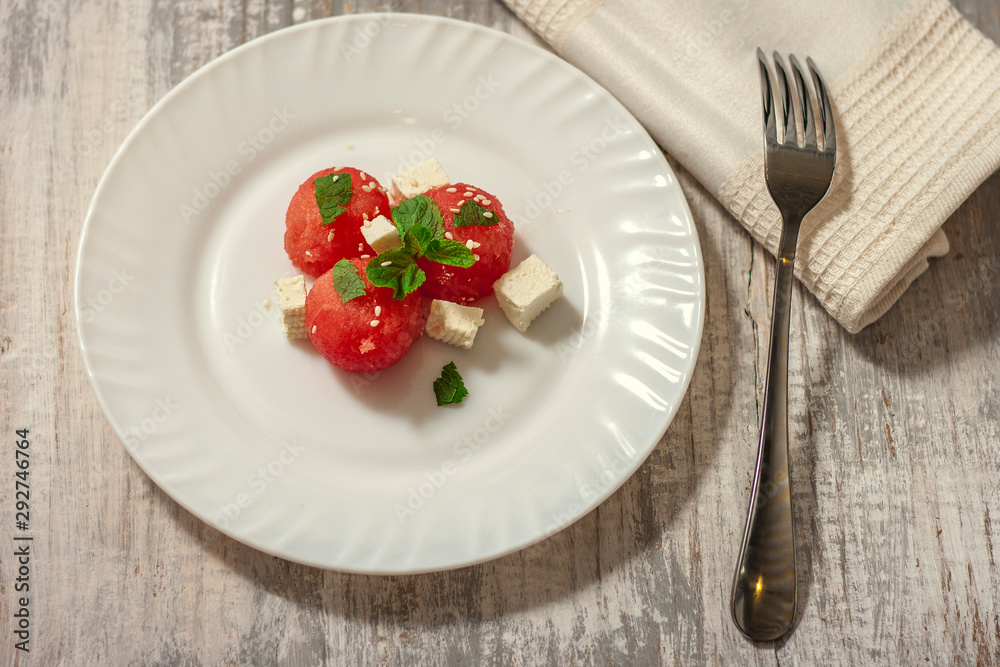 Salad of watermelon balls, feta cheese and mint, sprinkled with sesame seeds in a white plate. Close up