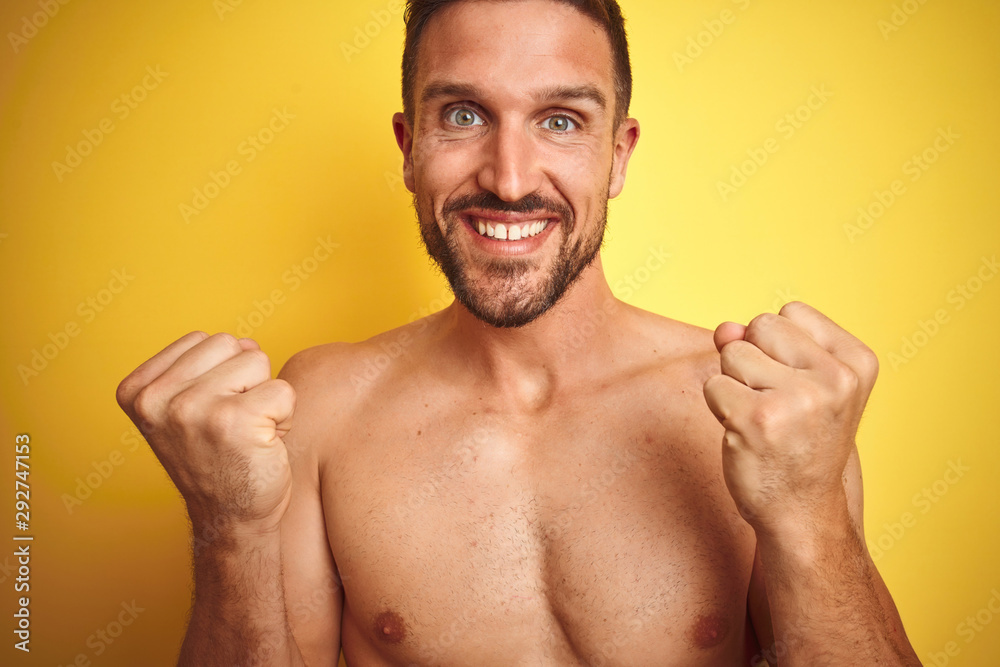 Sexy young shirtless man showing nude fitness chest over yellow isolated background celebrating surprised and amazed for success with arms raised and open eyes. Winner concept.