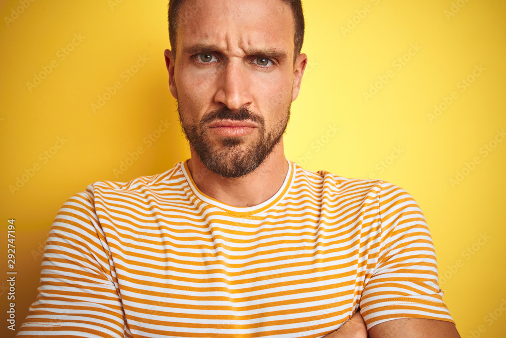 Close up of young handsome man wearing casual t-shirt over yellow isolated background skeptic and nervous, disapproving expression on face with crossed arms. Negative person. Close up of young handsome man wearing casual t-shirt over yellow isolated background skeptic and nervous, disapproving expression on face with crossed arms. Negative person.
