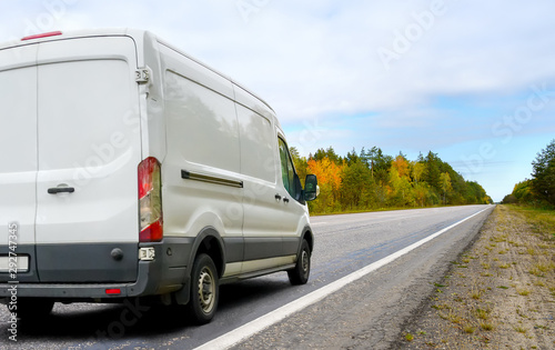 White van drives a country road on autumn landscape background photo