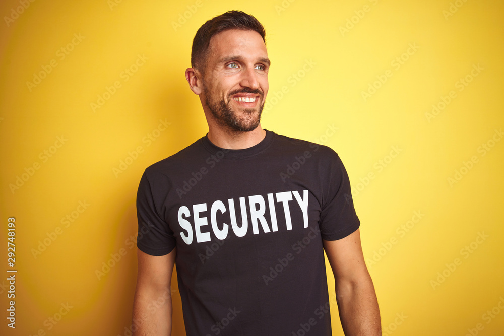 Young safeguard man wearing security uniform over yellow isolated background looking away to side with smile on face, natural expression. Laughing confident. Young safeguard man wearing security uniform over yellow isolated background looking away to side with smile on face, natural expression. Laughing confident.