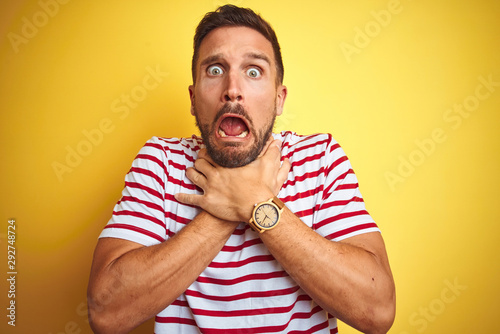 Young handsome man wearing casual red striped t-shirt over yellow isolated background shouting and suffocate because painful strangle. Health problem. Asphyxiate and suicide concept.