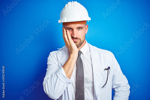 Young handsome engineer man wearing safety helmet over blue isolated background thinking looking tired and bored with depression problems with crossed arms.