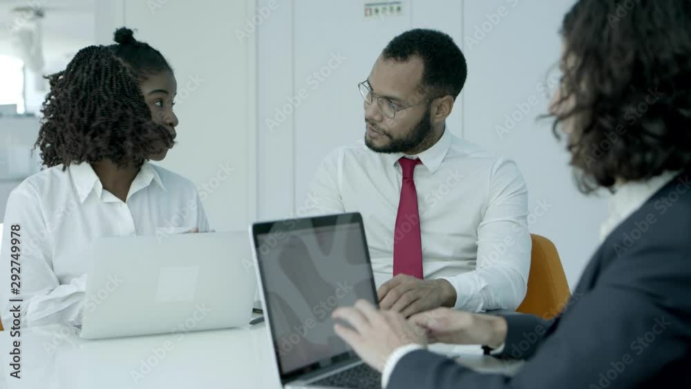 Smiling business people in office. Multiethnic male and female business colleagues talking and using laptops during meeting. Teamwork concept Smiling business people in office. Multiethnic male and female business colleagues talking and using laptops during meeting. Teamwork concept