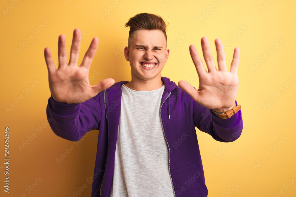 Young handsome man wearing purple sweatshirt standing over isolated yellow background afraid and terrified with fear expression stop gesture with hands, shouting in shock. Panic concept. Young handsome man wearing purple sweatshirt standing over isolated yellow background afraid and terrified with fear expression stop gesture with hands, shouting in shock. Panic concept.