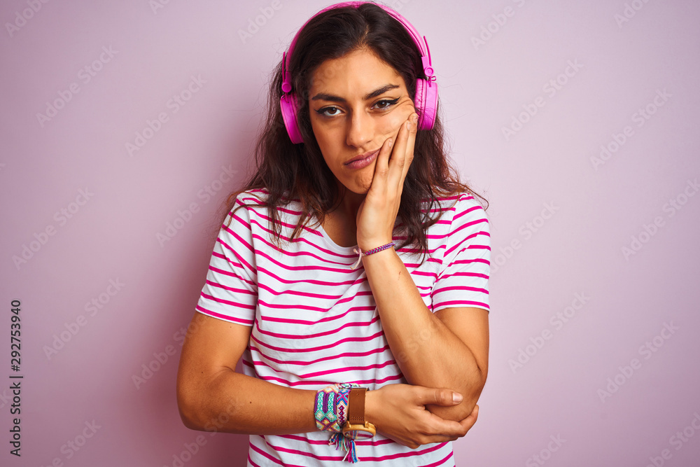 Young beautiful woman listening to music using headphones over isolated pink background thinking looking tired and bored with depression problems with crossed arms.