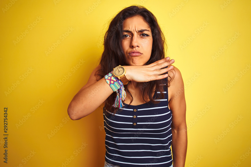 Young beautiful woman wearing striped t-shirt standing over isolated yellow background cutting throat with hand as knife, threaten aggression with furious violence Young beautiful woman wearing striped t-shirt standing over isolated yellow background cutting throat with hand as knife, threaten aggression with furious violence