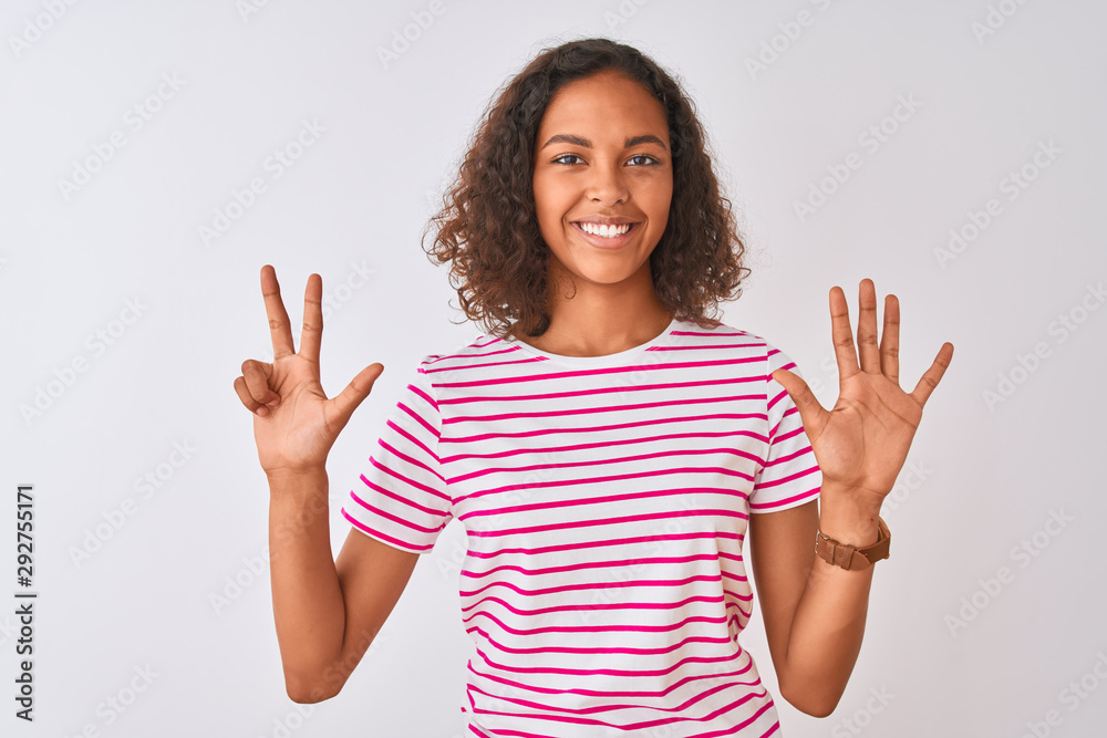 Young brazilian woman wearing pink striped t-shirt standing over isolated white background showing and pointing up with fingers number eight while smiling confident and happy. Young brazilian woman wearing pink striped t-shirt standing over isolated white background showing and pointing up with fingers number eight while smiling confident and happy.