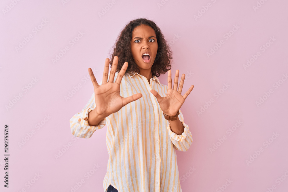 Young brazilian woman wearing striped shirt standing over isolated pink background afraid and terrified with fear expression stop gesture with hands, shouting in shock. Panic concept. Young brazilian woman wearing striped shirt standing over isolated pink background afraid and terrified with fear expression stop gesture with hands, shouting in shock. Panic concept.