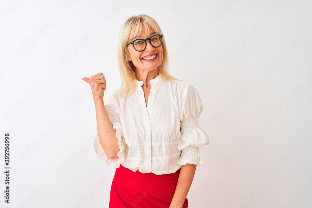 Middle age businesswoman wearing shirt and glasses standing over isolated white background smiling with happy face looking and pointing to the side with thumb up. Middle age businesswoman wearing shirt and glasses standing over isolated white background smiling with happy face looking and pointing to the side with thumb up.