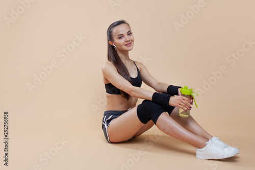 Young athletic girl brunette with black knee-pads sits on the floor, rests after a workout, takes a break.