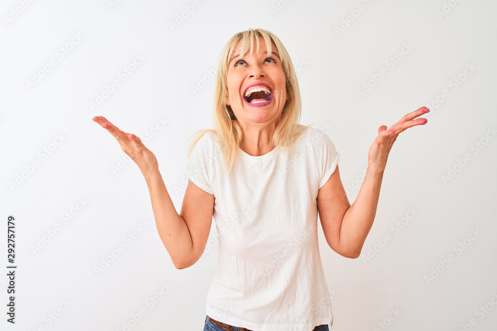 Middle age woman wearing casual t-shirt standing over isolated white background celebrating mad and crazy for success with arms raised and closed eyes screaming excited. Winner concept Middle age woman wearing casual t-shirt standing over isolated white background celebrating mad and crazy for success with arms raised and closed eyes screaming excited. Winner concept