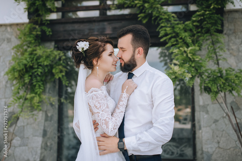 Beautiful newlyweds are hugging against the background of an old house in nature. Wedding portrait of a bearded stylish groom and pretty brunette bride. Photography and concept.