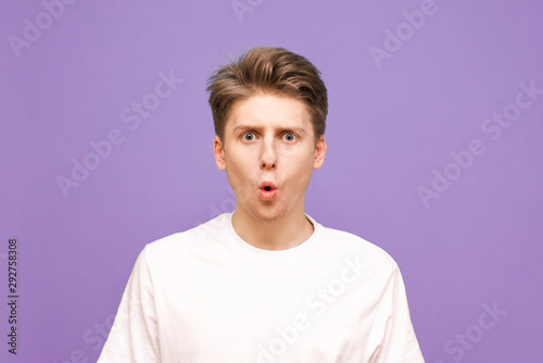 Close up portrait of an adorable guy on a purple background, look into the camera with an open mouth. Emotional young man is isolated on a blue background.