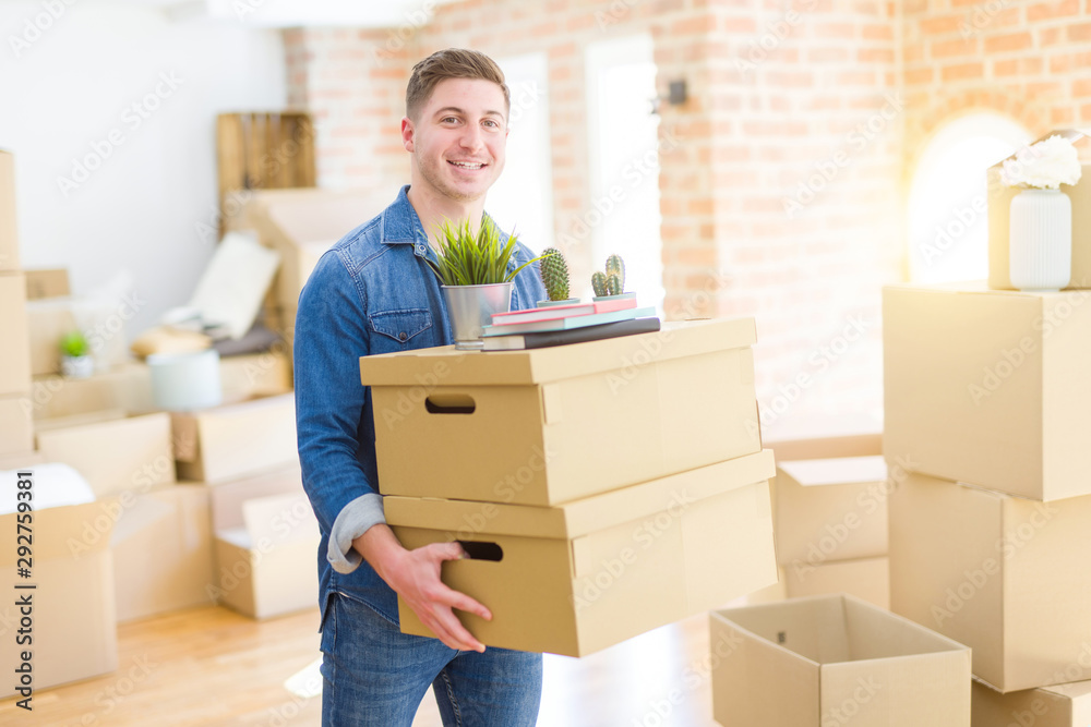 Handsome young man smiling happy moving to a new home, very excited holding cardboard boxes at new apartment Handsome young man smiling happy moving to a new home, very excited holding cardboard boxes at new apartment