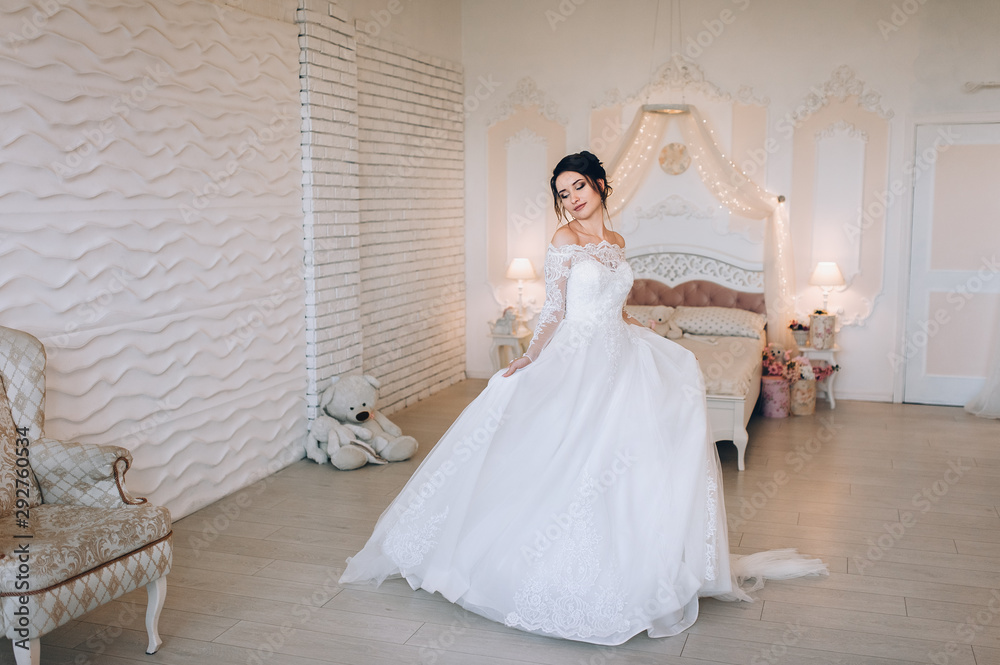 A beautiful bride is spinning and dancing, holding on to a dress. Wedding portrait of a cute girl in a room, studio on the background of wall and bed. Photography and concept. Wedding decorations. A beautiful bride is spinning and dancing, holding on to a dress. Wedding portrait of a cute girl in a room, studio on the background of wall and bed. Photography and concept. Wedding decorations.