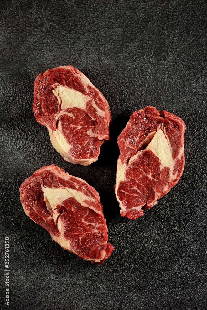 Obraz premium Three raw fresh beef steaks rib eye on a black background. Top view. Copy space. 