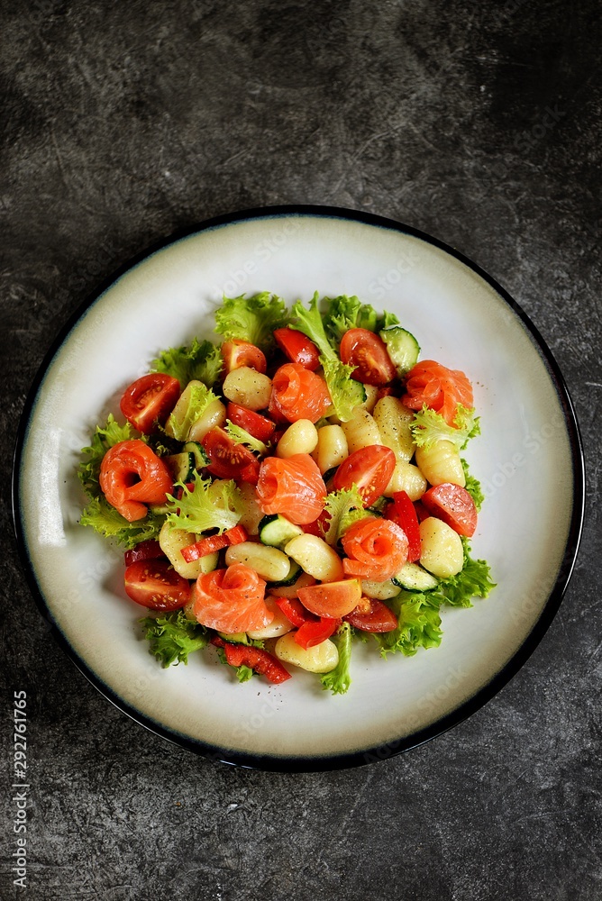Healthy potato gnocchi salad with cherry tomatoes, cucumber, bell pepper, slightly salted salmon, olive oil and lettuce. Top view. Healthy potato gnocchi salad with cherry tomatoes, cucumber, bell pepper, slightly salted salmon, olive oil and lettuce. Top view.