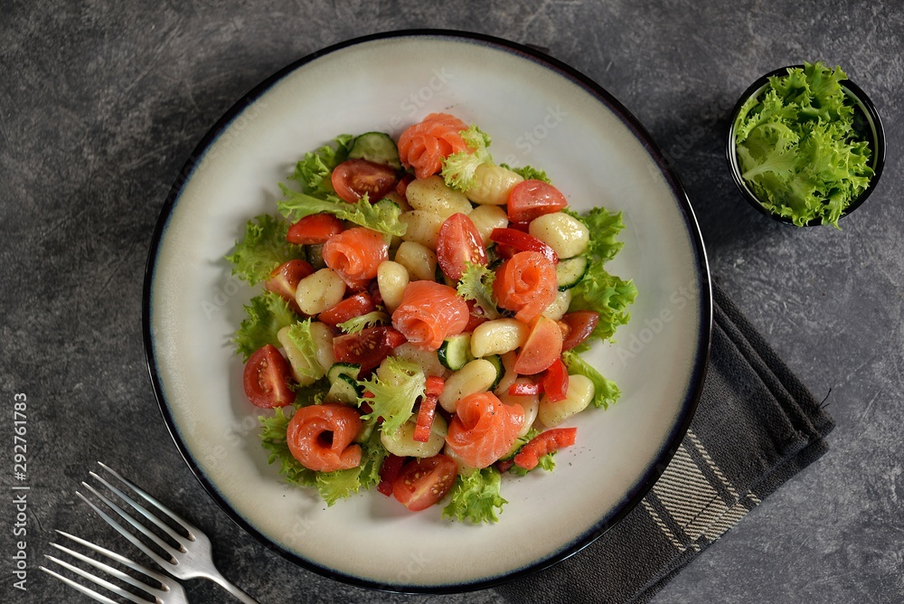 Healthy potato gnocchi salad with cherry tomatoes, cucumber, bell pepper, slightly salted salmon, olive oil and lettuce. Top view. Healthy potato gnocchi salad with cherry tomatoes, cucumber, bell pepper, slightly salted salmon, olive oil and lettuce. Top view.