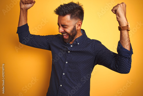 Young handsome indian businessman wearing shirt over isolated yellow background very happy and excited doing winner gesture with arms raised, smiling and screaming for success. Celebration concept.