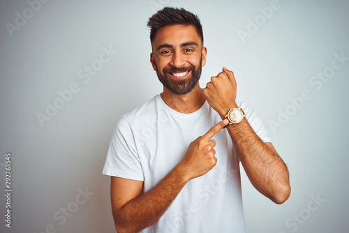 Young indian man wearing t-shirt standing over isolated white background In hurry pointing to watch time, impatience, looking at the camera with relaxed expression photo