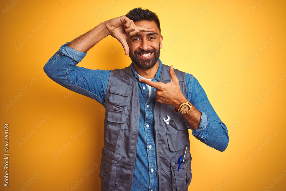Handsome indian technician man wearing uniform over isolated yellow background smiling making frame with hands and fingers with happy face. Creativity and photography concept. Handsome indian technician man wearing uniform over isolated yellow background smiling making frame with hands and fingers with happy face. Creativity and photography concept.
