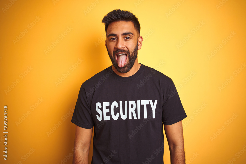 Arab indian hispanic safeguard man wearing security uniform over isolated yellow background sticking tongue out happy with funny expression. Emotion concept. Arab indian hispanic safeguard man wearing security uniform over isolated yellow background sticking tongue out happy with funny expression. Emotion concept.