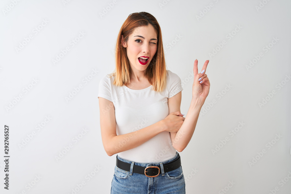 Beautiful redhead woman wearing casual t-shirt standing over isolated white background smiling with happy face winking at the camera doing victory sign. Number two. Beautiful redhead woman wearing casual t-shirt standing over isolated white background smiling with happy face winking at the camera doing victory sign. Number two.