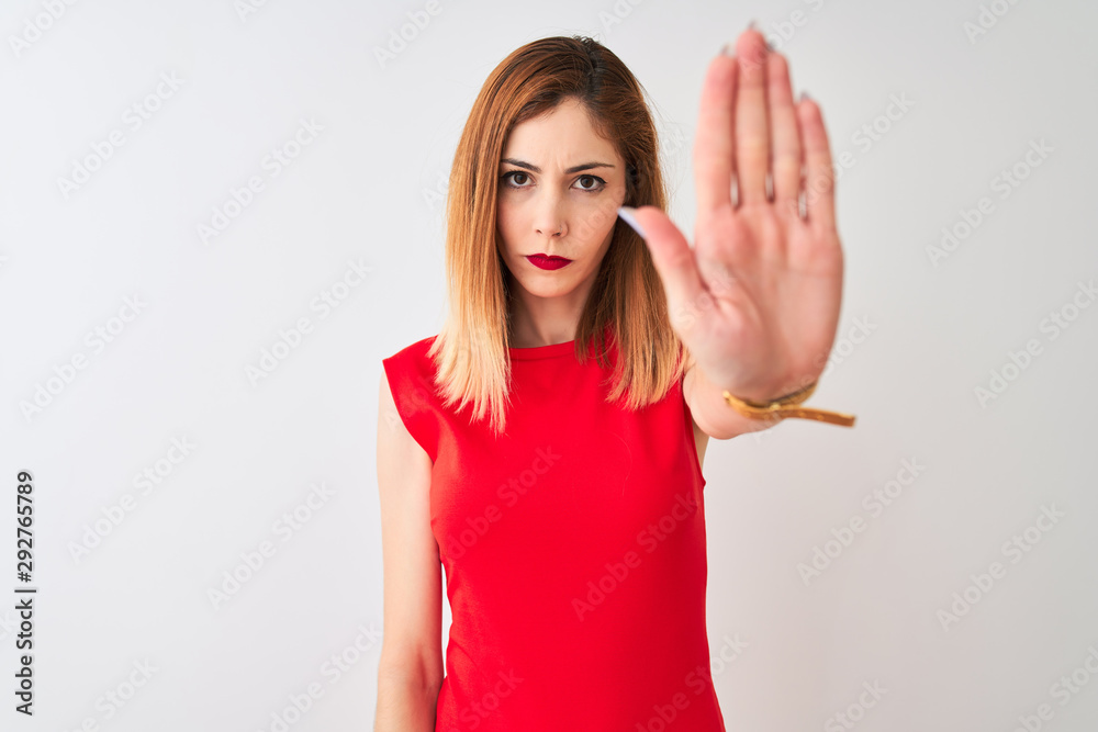 Fototapeta premium Redhead businesswoman wearing elegant red dress standing over isolated white background doing stop sing with palm of the hand. Warning expression with negative and serious gesture on the face.