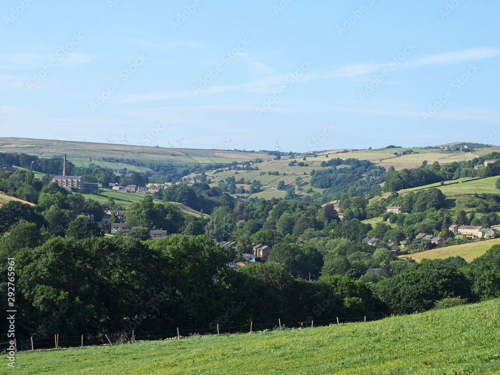 a scenic view of the calder valley with the village of luddenden between trees and surrounding hillside fields