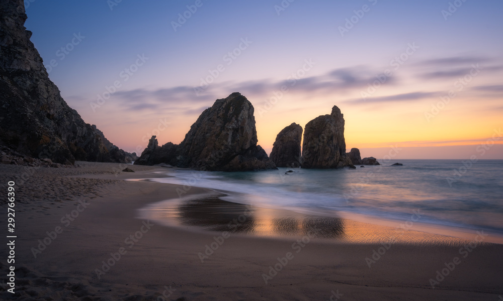 Epic Ursa Beach with rock silhouette and reflection against golden sunset light. Cabo da Roca, Sintra at Atlantic Ocean coast in Portugal