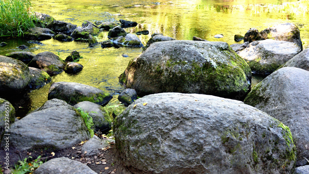 sun reflects in river makes water surface bright yellow, dark stones in front sun reflects in river makes water surface bright yellow, dark stones in front
