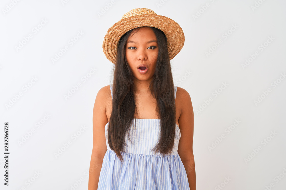 Young chinese woman wearing striped dress and hat standing over isolated white background afraid and shocked with surprise expression, fear and excited face. Young chinese woman wearing striped dress and hat standing over isolated white background afraid and shocked with surprise expression, fear and excited face.