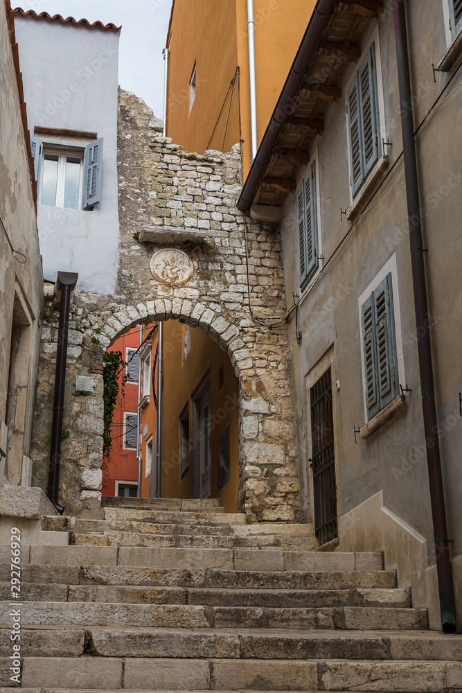 Looking up some steps in a narrow street of Rovinj, Croatia, towards a limestone built arch.