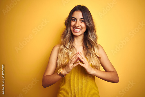 Young beautiful woman wearing t-shirt over yellow isolated background Hands together and fingers crossed smiling relaxed and cheerful. Success and optimistic