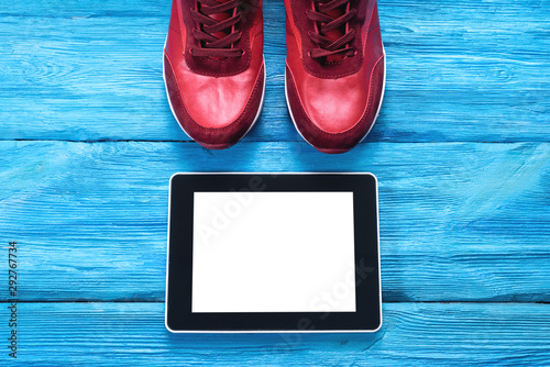 Digital tablet with blank screen and pair of new red sport sneakers on blue wooden background. photo